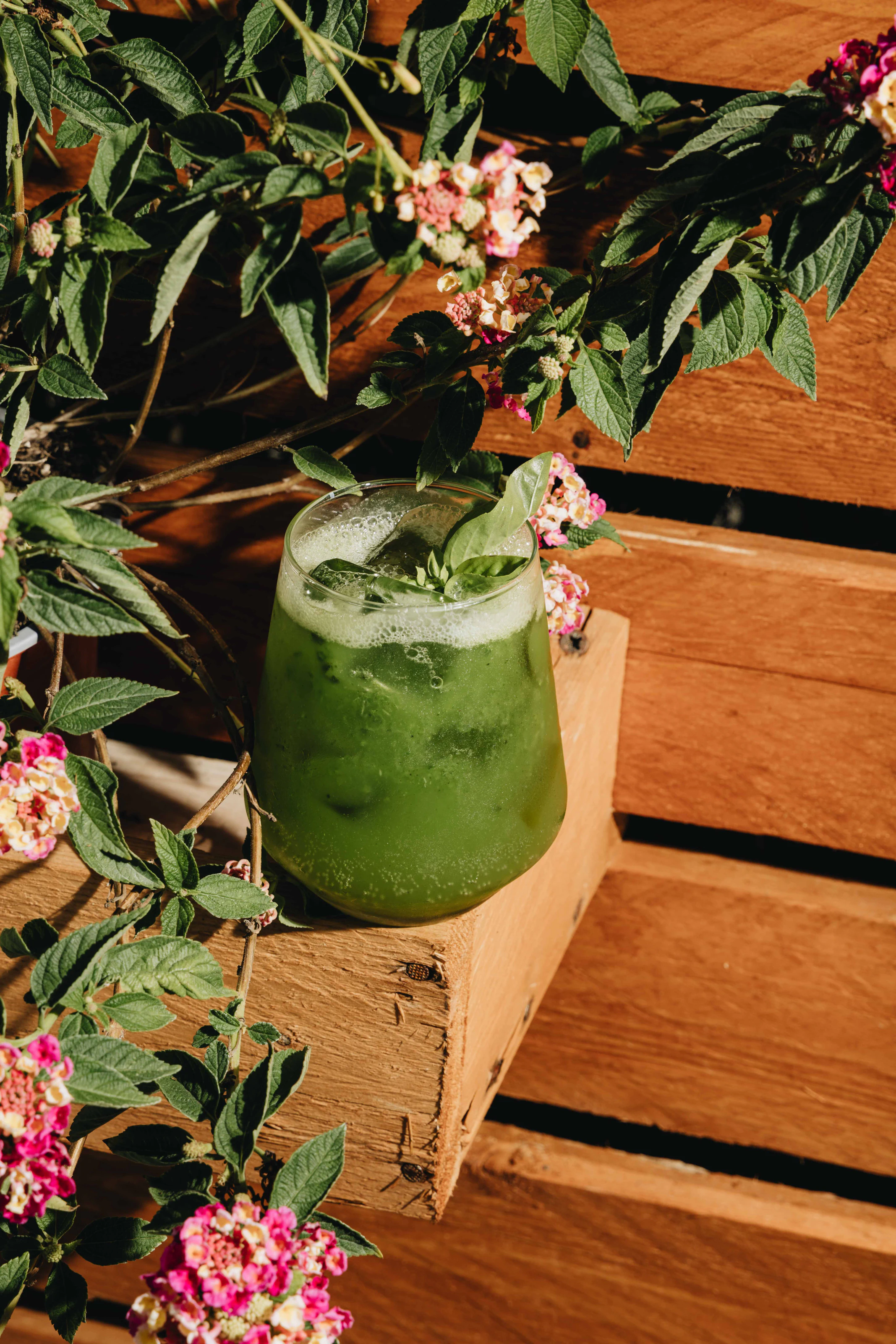 Cocktail verde fotografato tra legno e fiori